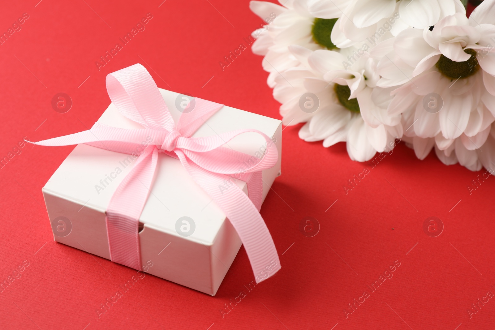 Photo of Gift box with bow and flowers on red background