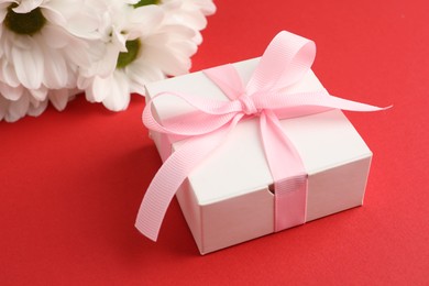 Photo of Gift box with bow and flowers on red background