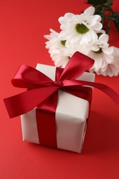 Photo of Gift box with bow and flowers on red background