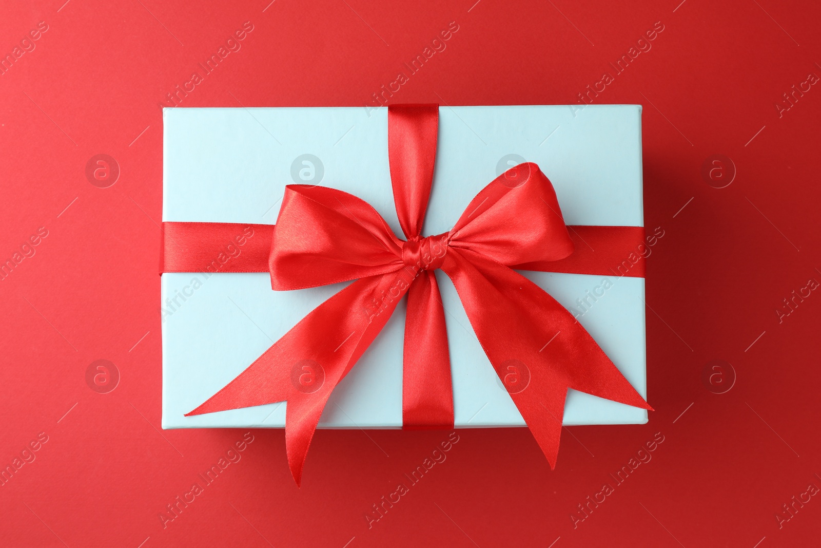 Photo of Gift box with bow on red background, top view