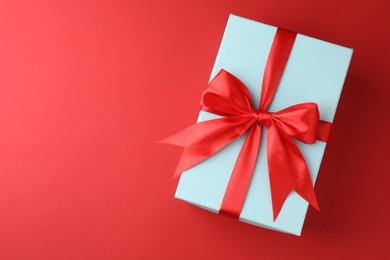 Gift box with bow on red background, top view. Space for text