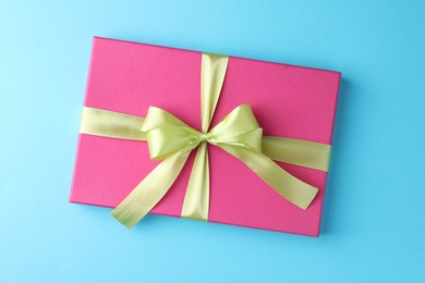 Gift box with bow on light blue background, top view