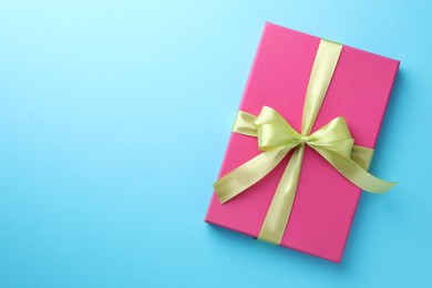 Photo of Gift box with bow on light blue background, top view. Space for text