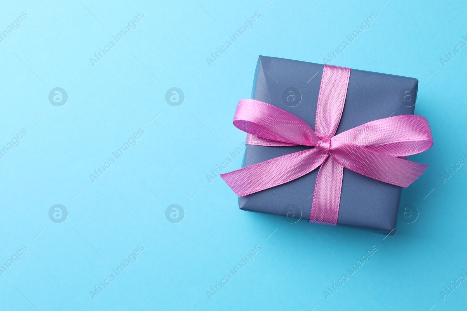 Photo of Gift box with bow on light blue background, top view. Space for text