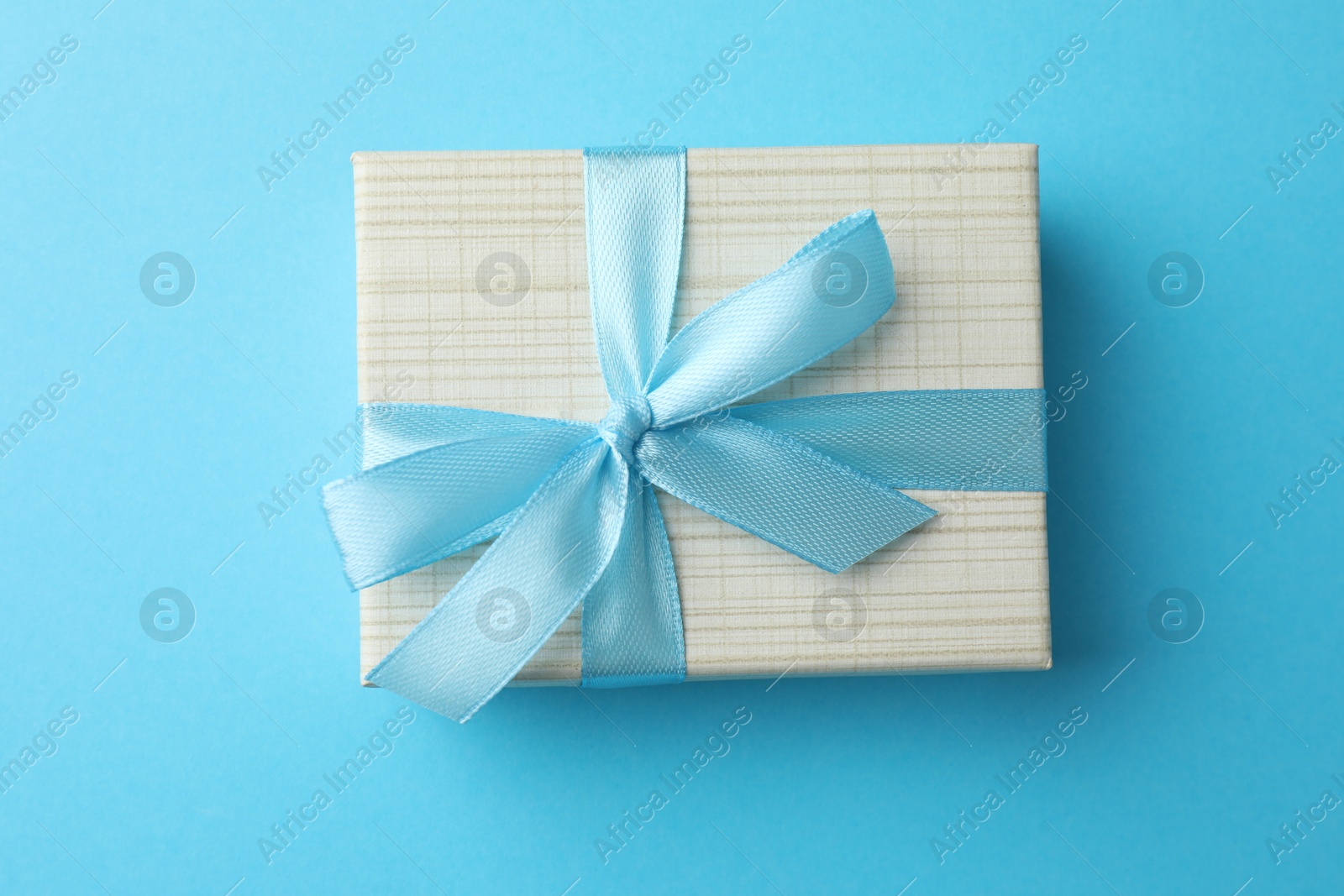 Photo of Gift box with bow on light blue background, top view