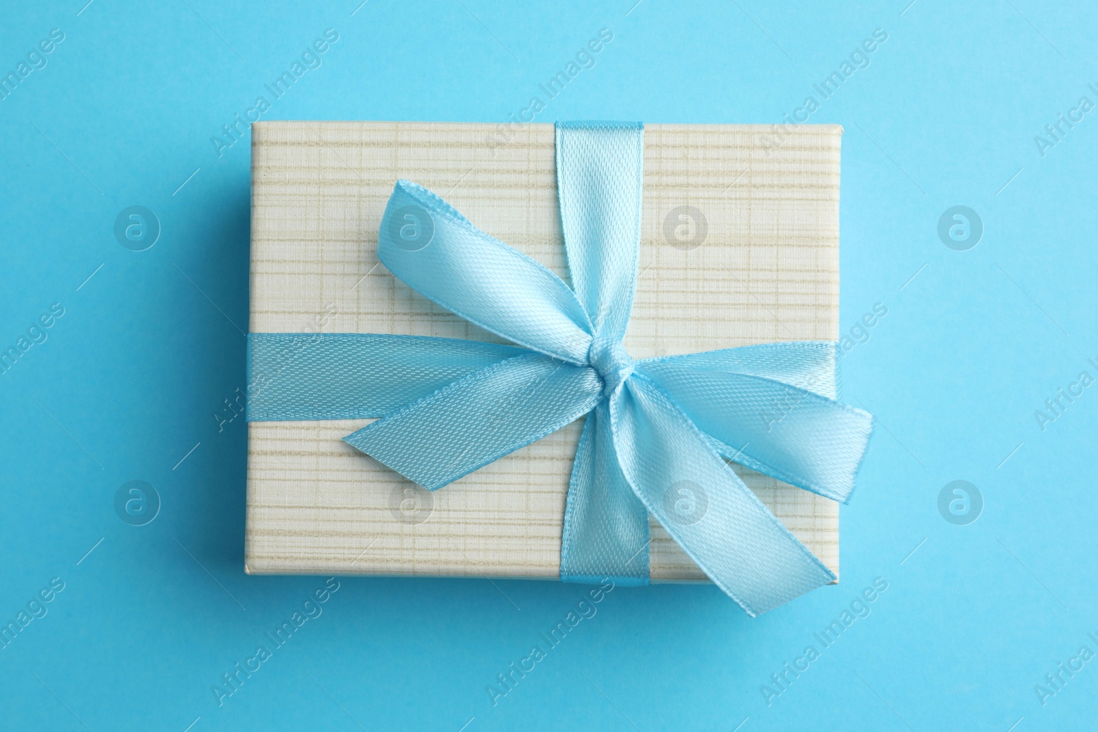 Photo of Gift box with bow on light blue background, top view