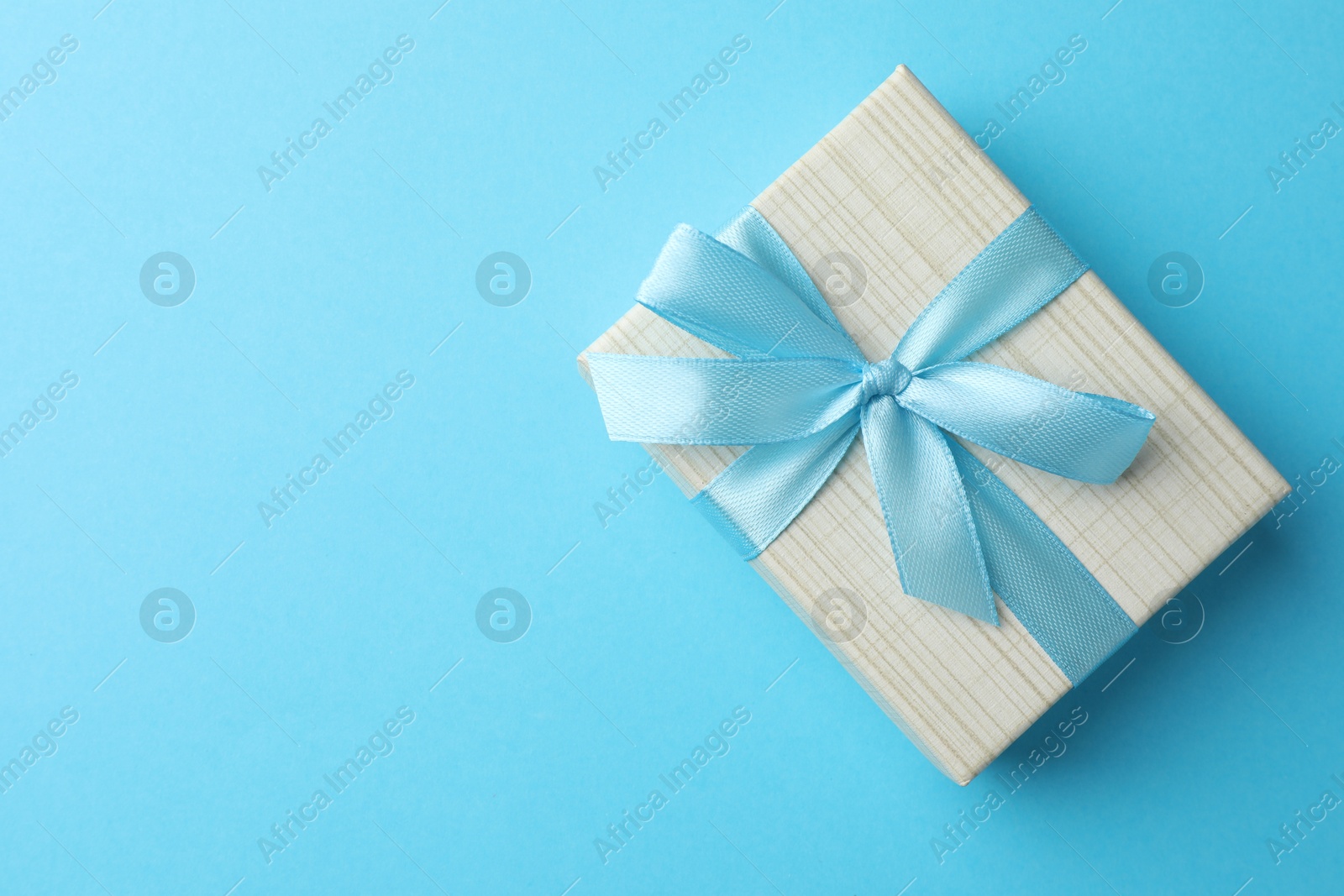 Photo of Gift box with bow on light blue background, top view. Space for text