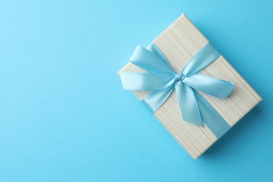 Photo of Gift box with bow on light blue background, top view. Space for text