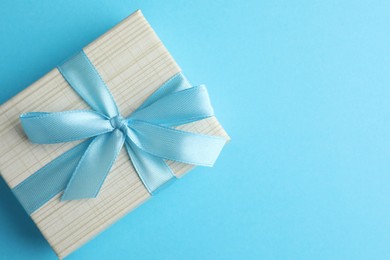 Photo of Gift box with bow on light blue background, top view. Space for text