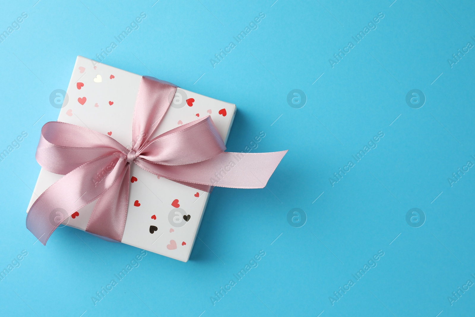 Photo of Gift box with bow on light blue background, top view. Space for text