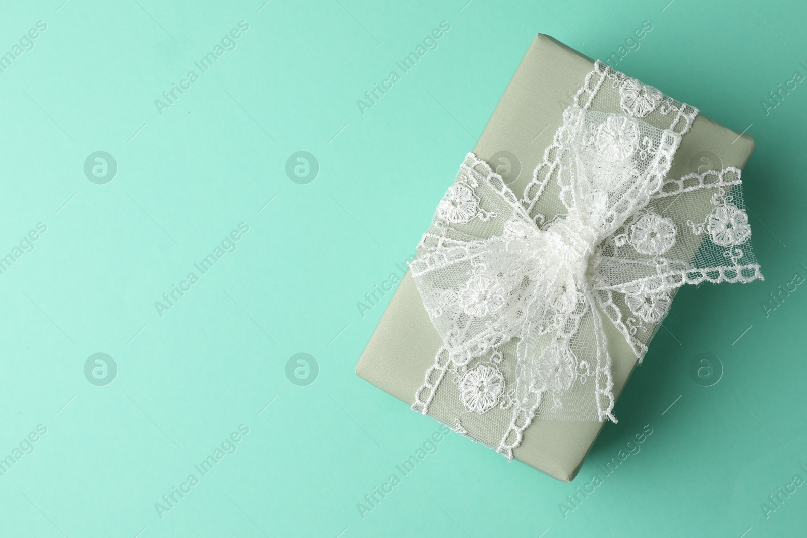 Photo of Gift box with bow on turquoise background, top view. Space for text