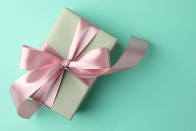 Photo of Gift box with bow on turquoise background, top view