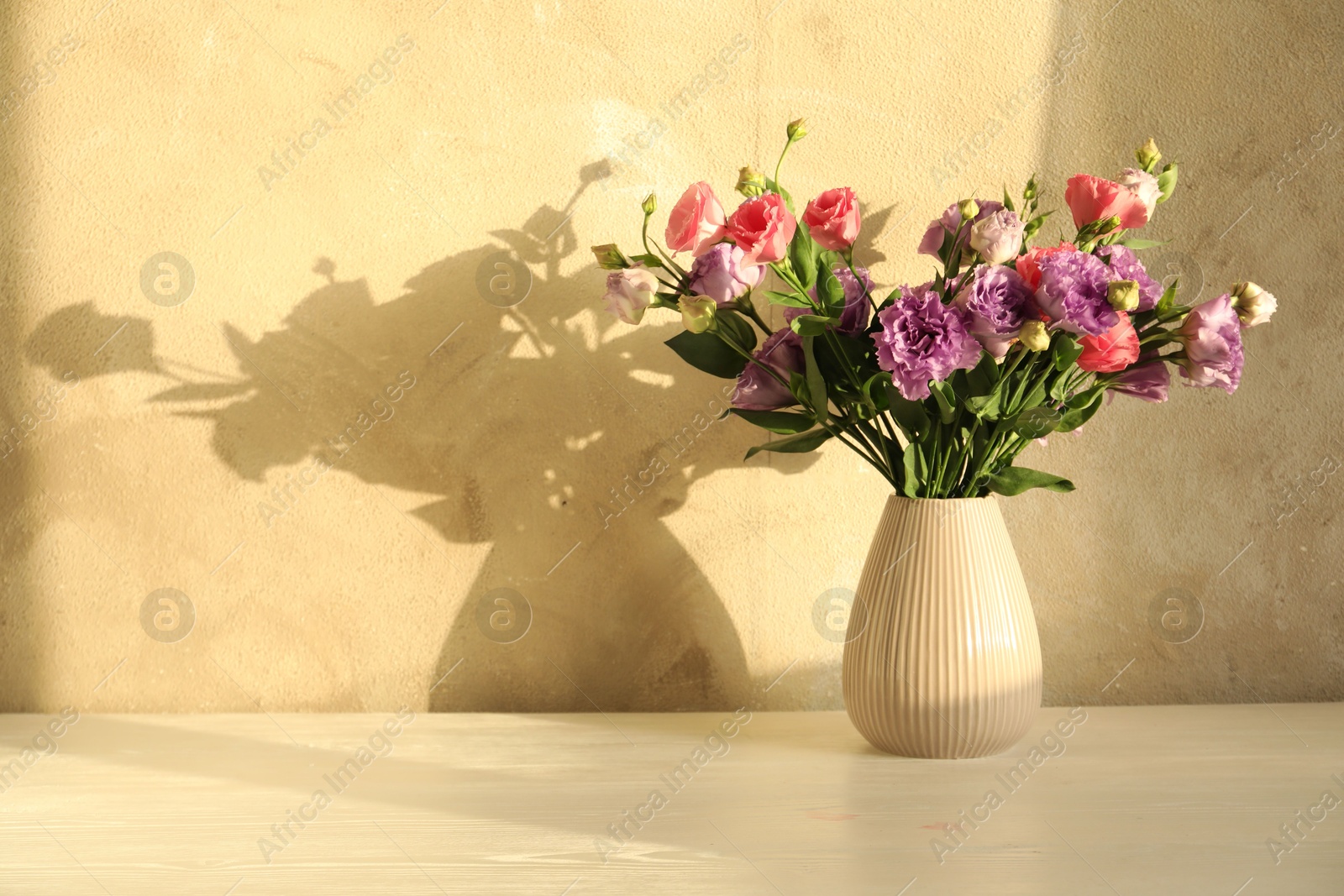 Photo of Vase with beautiful eustoma flowers on white wooden table, space for text