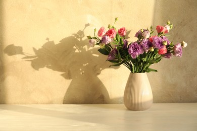 Vase with beautiful eustoma flowers on white wooden table, space for text