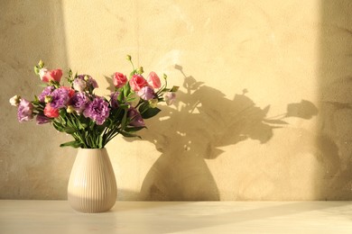 Vase with beautiful eustoma flowers on white wooden table, space for text