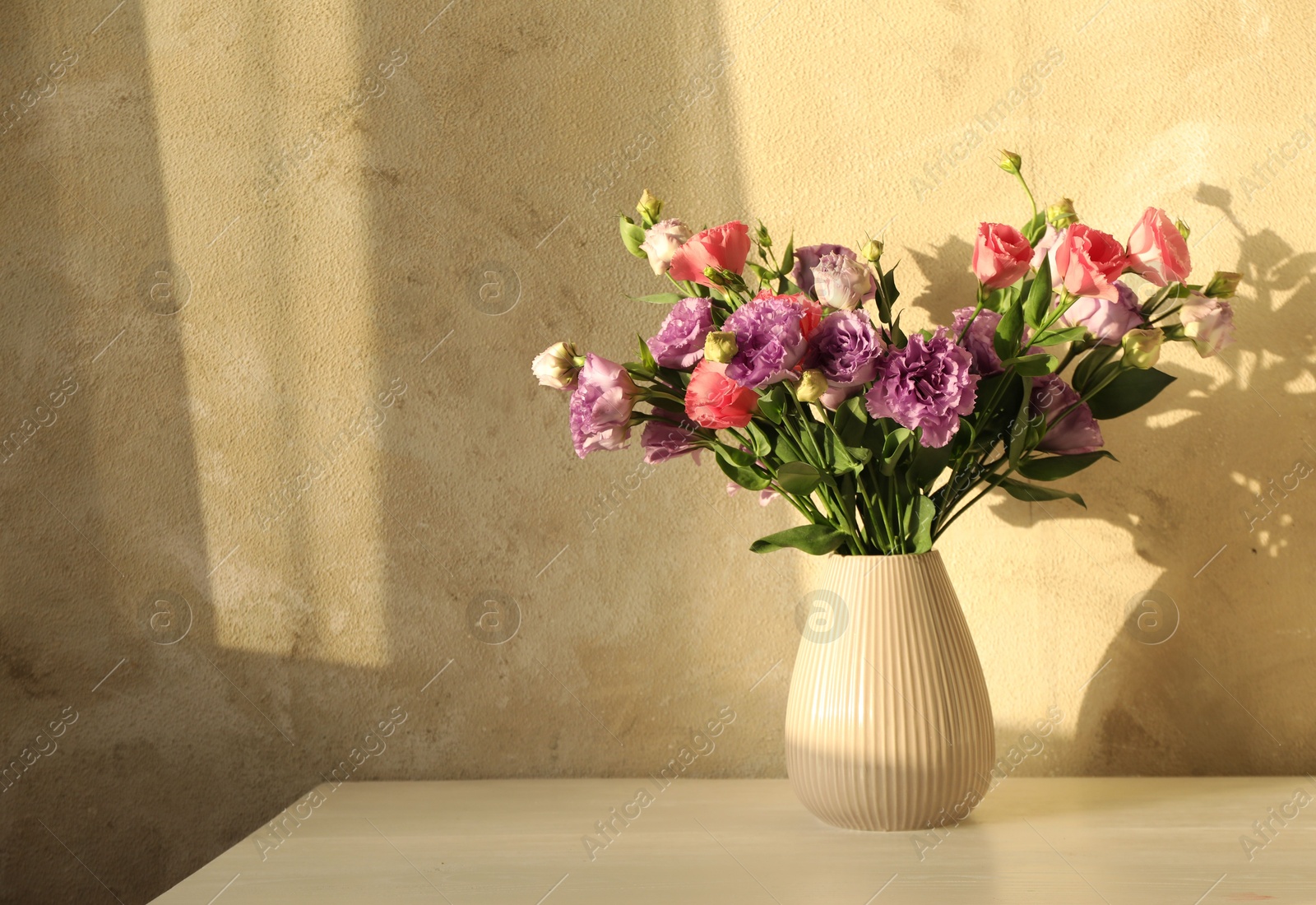 Photo of Vase with beautiful eustoma flowers on white wooden table, space for text