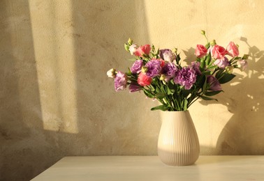 Vase with beautiful eustoma flowers on white wooden table, space for text