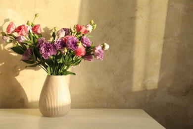 Vase with beautiful eustoma flowers on white wooden table, space for text