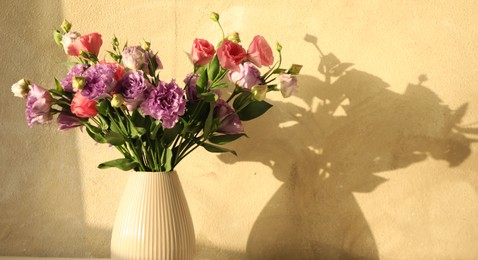 Vase with beautiful eustoma flowers near beige wall, closeup. Space for text