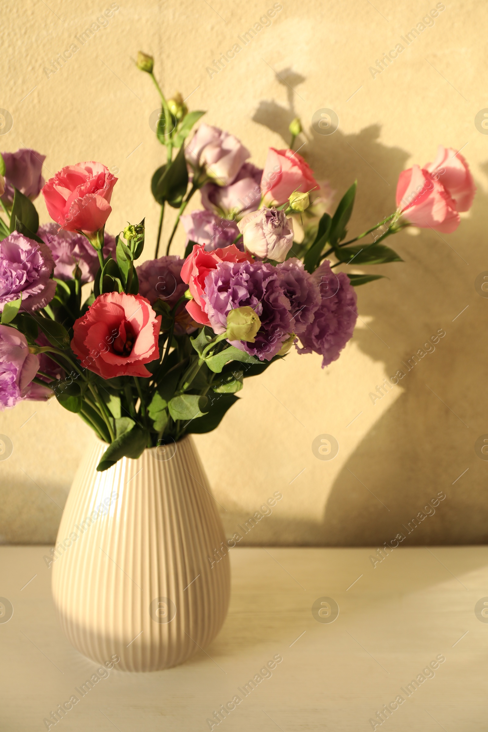 Photo of Vase with beautiful eustoma flowers on white wooden table