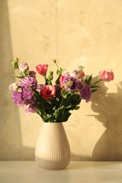 Vase with beautiful eustoma flowers on white wooden table