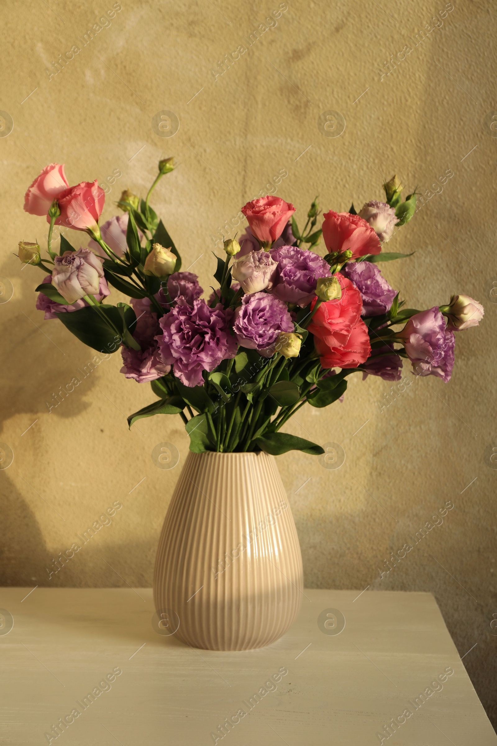 Photo of Vase with beautiful eustoma flowers on white wooden table