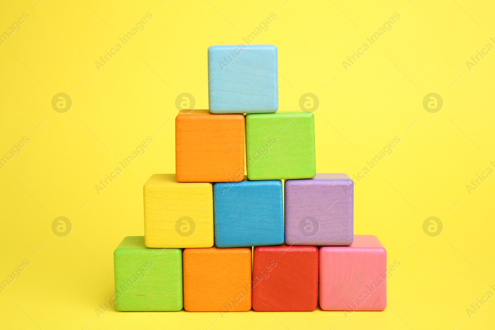 Photo of Pyramid of colorful cubes on yellow background