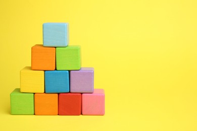 Photo of Pyramid of colorful cubes on yellow background. Space for text