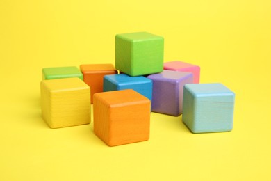 Photo of Many wooden colorful cubes on yellow background