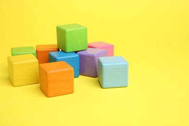 Photo of Many wooden colorful cubes on yellow background