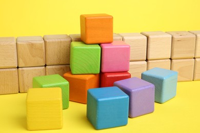 Photo of Many wooden colorful cubes on yellow background