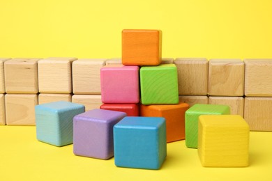 Photo of Many wooden colorful cubes on yellow background