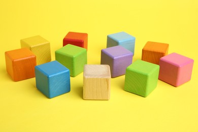 Photo of Many wooden colorful cubes on yellow background