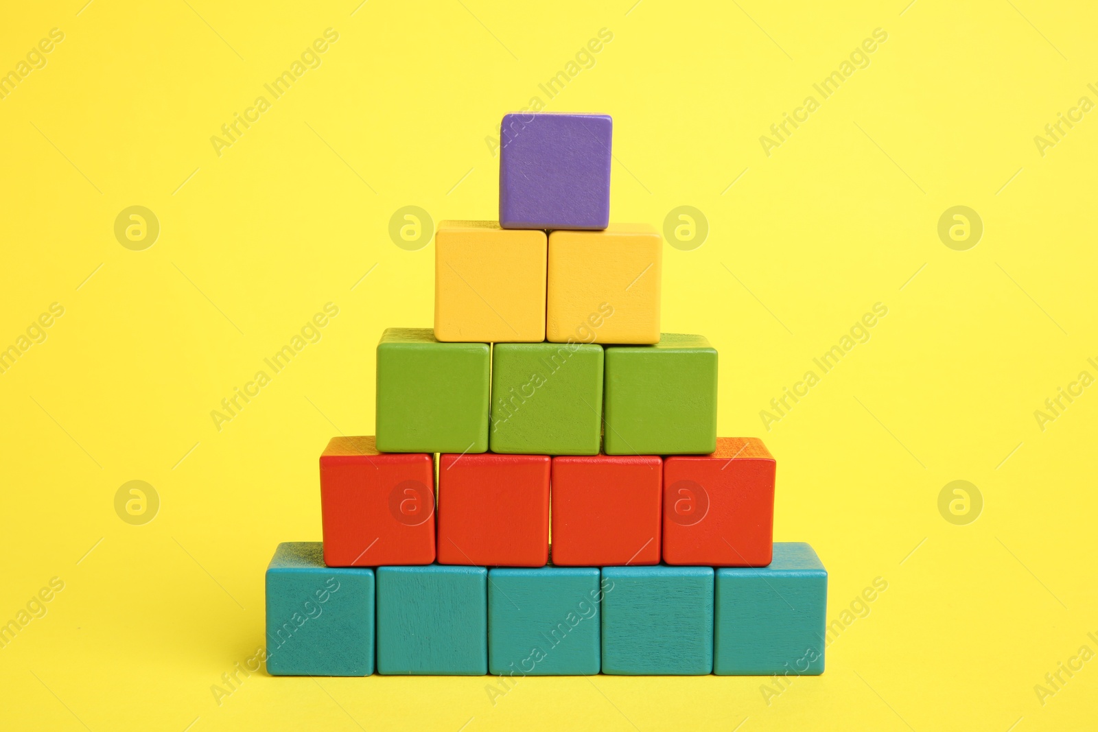 Photo of Pyramid of colorful cubes on yellow background