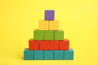 Photo of Pyramid of colorful cubes on yellow background