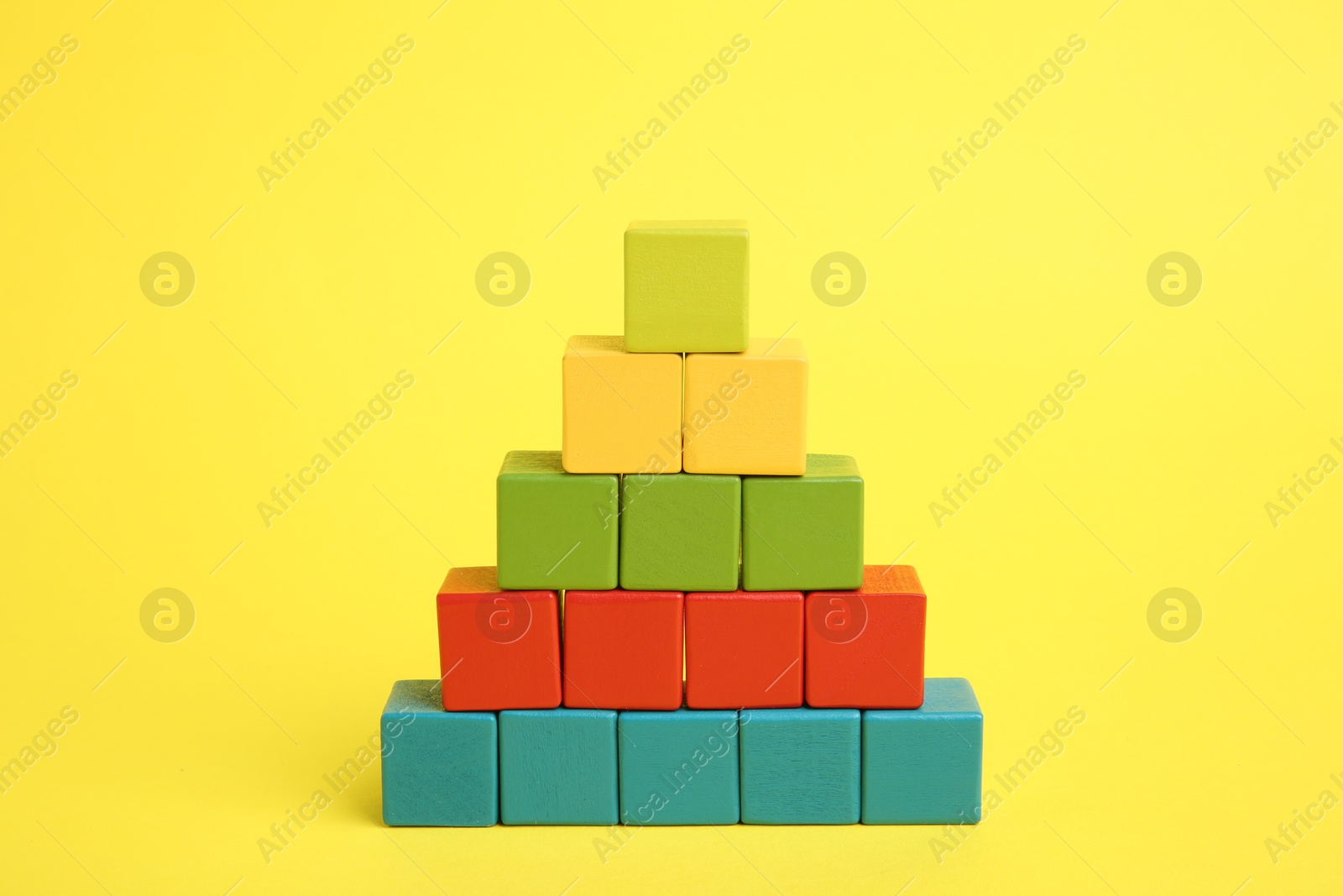 Photo of Pyramid of colorful cubes on yellow background