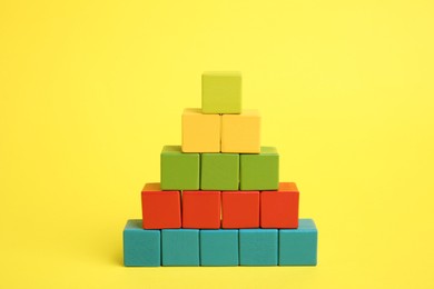 Photo of Pyramid of colorful cubes on yellow background