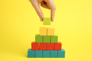 Photo of Woman building pyramid of cubes on yellow background, closeup