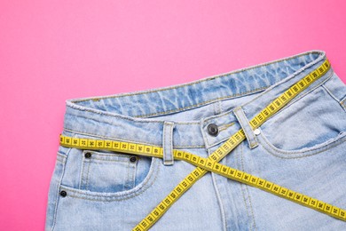 Photo of Jeans and measuring tape on pink background, top view