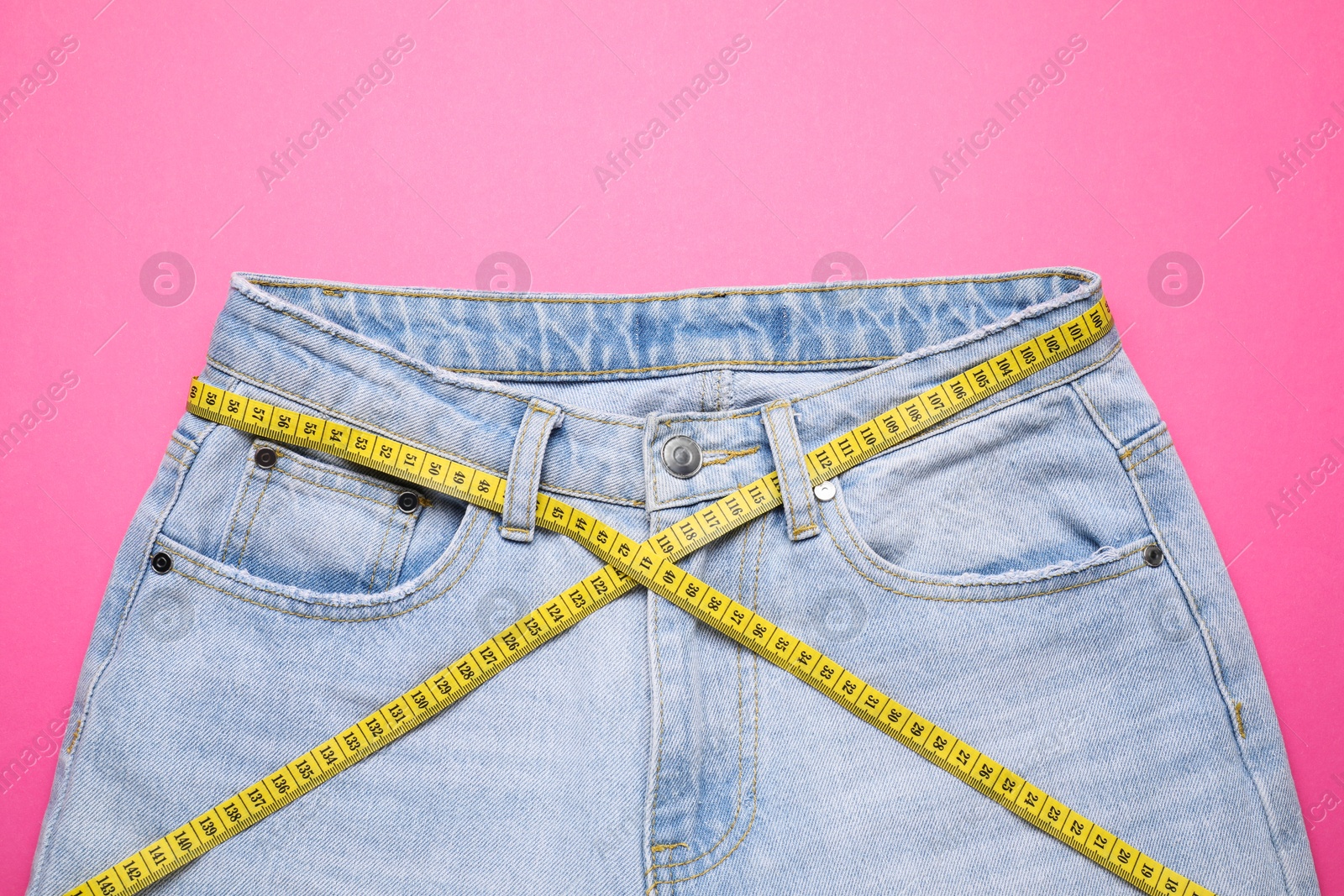 Photo of Jeans and measuring tape on pink background, top view