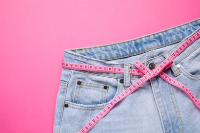 Photo of Jeans and measuring tape on pink background, top view