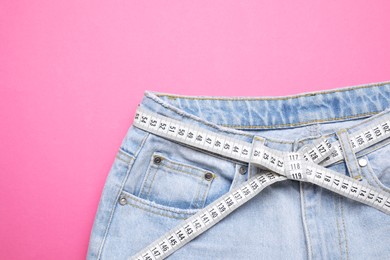 Photo of Jeans and measuring tape on pink background, top view