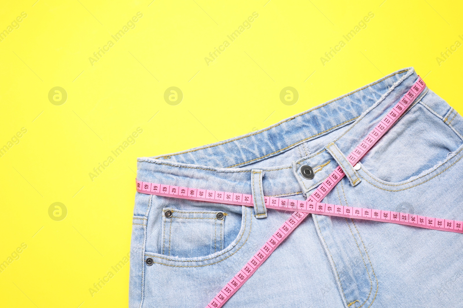 Photo of Jeans and measuring tape on yellow background, top view