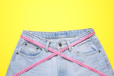 Photo of Jeans and measuring tape on yellow background, top view