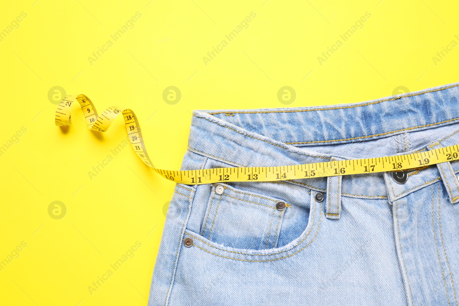 Photo of Jeans and measuring tape on yellow background, top view