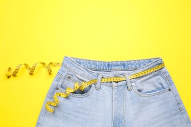 Photo of Jeans and measuring tape on yellow background, top view