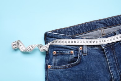 Photo of Jeans and measuring tape on light blue background, top view. Space for text