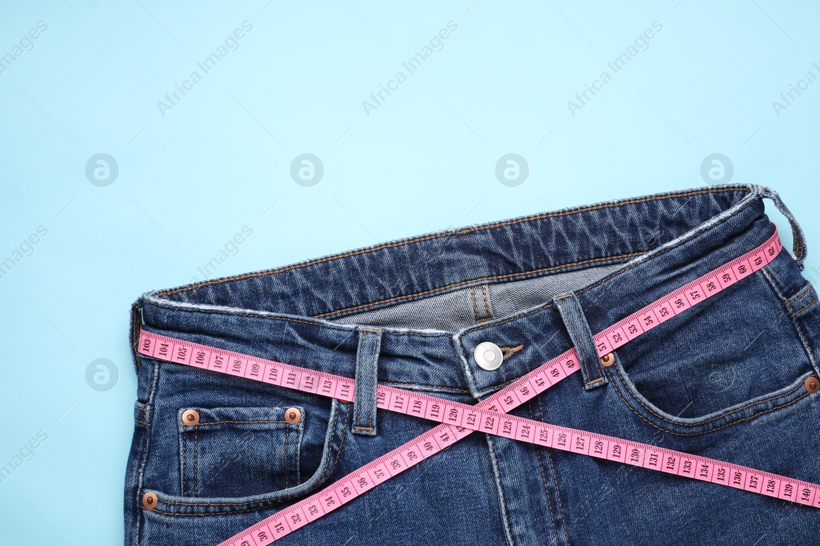 Photo of Jeans and measuring tape on light blue background, top view. Space for text