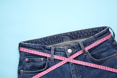 Photo of Jeans and measuring tape on light blue background, top view. Space for text