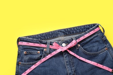 Photo of Jeans and measuring tape on yellow background, top view